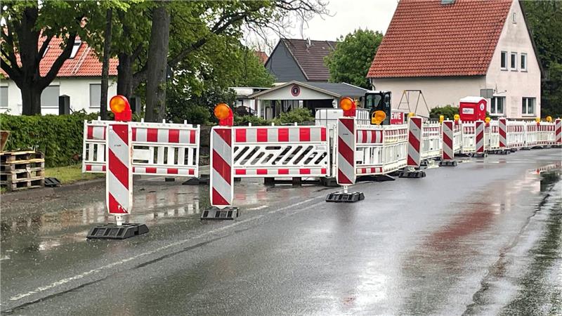 Straßensperren mit rot-weißen Warnbaken und Blinklichtern auf nasser Straße in Wohngegend