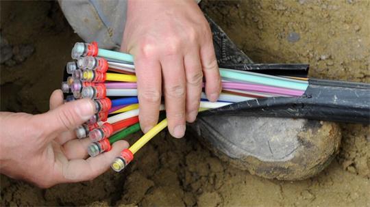 Ein Mann fächert ein Glasfaser-Kabel mit farbigen Einzelsträngen auseinander.