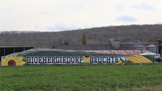 Langgestrecktes Gebäude mit bemalter Fassade, auf der die Worte 'BIOENERGIEDORF BEUCHTE' zwischen Sonnenblumen und Maiskolben stehen