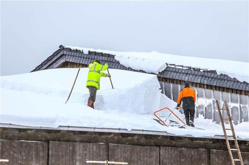 Harz: weitgehend verschont: Wenig Unfälle, Probleme bei der Bahn Zwei Männer schieben Schnee von einem Dach.