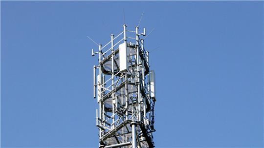 Nahaufnahme eines Sendemasts mit mehreren Antennen und Metallstreben vor blauem Himmel