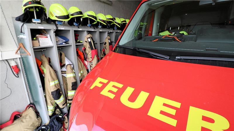 Einsatzkleidung hängt in einer Fahrzeughalle neben einem Einsatzfahrzeug der Feuerwehr.