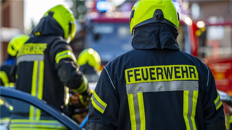 Das Bild zeigt Feuerwehrleute von hinten, die gerade im Einsatz sind, und ein Feuerwehrauto.