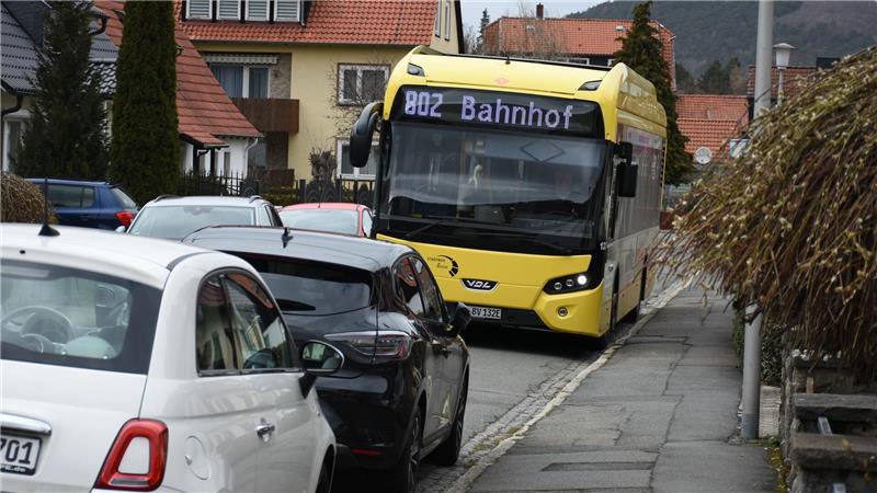 Ein Bus mit Endstation Bahnhof schlängelt sich zwischen zwei Autoreihen in einem Wohngebiet durch.