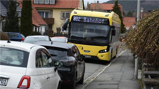 Ein Bus mit Endstation Bahnhof schlängelt sich zwischen zwei Autoreihen in einem Wohngebiet durch.