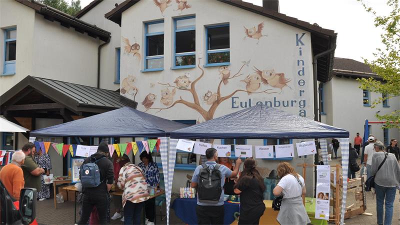 Kindergarten mit Ständen eines Festes im Vordergrund. 