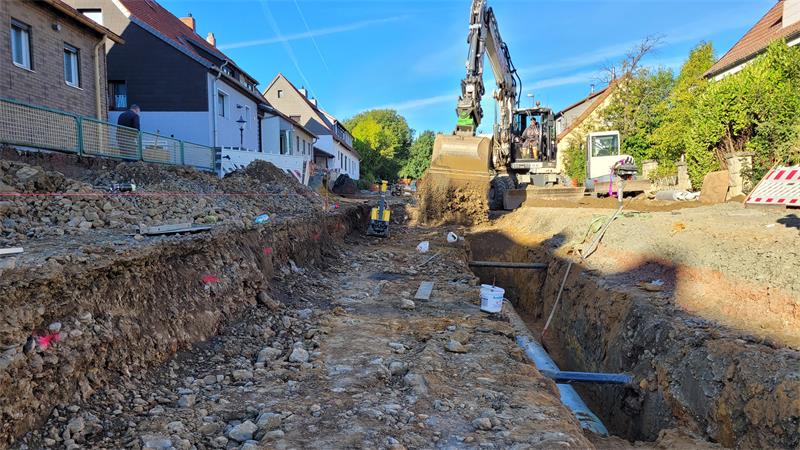 Ein Bagger füllt Erde in einen Graben auf einer Straßenbaustelle.