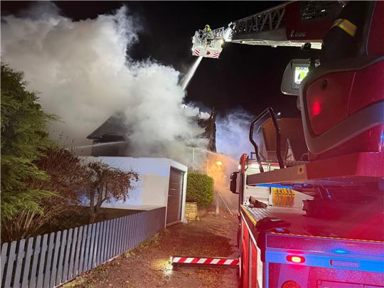 Ein Feuerwehrmann löscht von einer Drehleiter aus ein brennendes Gebäude.