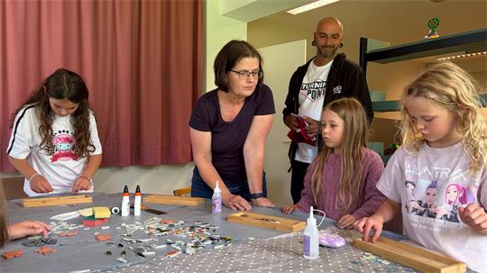 In der Stadt- und Schulbücherei fertigt Büchereileiterin Imke Koch im Rahmen des Ferienpass-Programms Mosaik-Tabletts mit Kindern. Im Hintergrund Stadtjugendpfleger Pavel Rössiger.