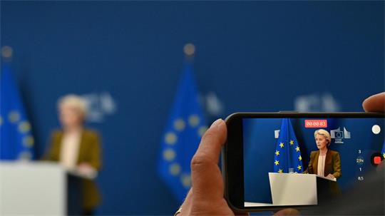 Blick auf das Display eines Smartphones, während einer Aufnahme von EU-Kommissionspräsidentin Ursula von der Leyen bei einem Pressestatement.