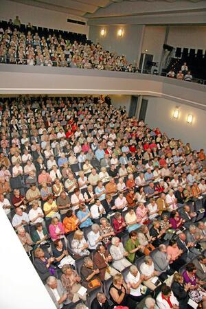 Voller Zuschauerraum in einem Theater oder Konzertsaal mit mehreren Sitzreihen und einem Balkon