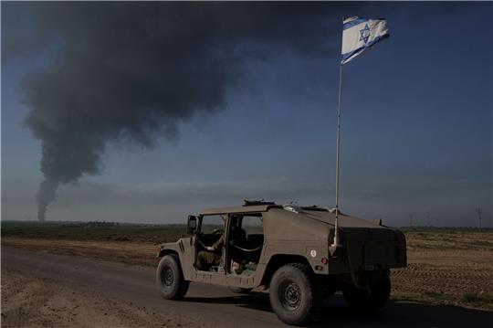 Israelische Soldaten in der Nähe der Grenze zwischen Israel und Gaza, während im Gazastreifen Rauch in den Himmel steigt.