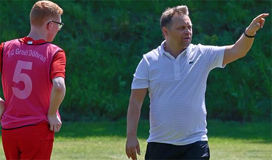 Ein Mann in weißem Poloshirt zeigt mit ausgestrecktem Arm nach rechts, daneben ein junger Fußballspieler in rotem Trikot mit der Aufschrift 'FC Groß Döhren' und der Nummer 5 auf dem Rücken. 