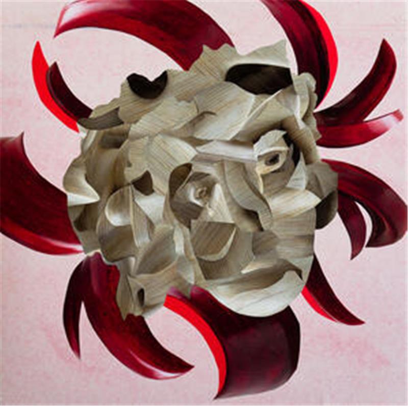 Skulptur eines menschlichen Gesichts aus hellbraunem Holz mit roten, geschwungenen Elementen im Hintergrund.