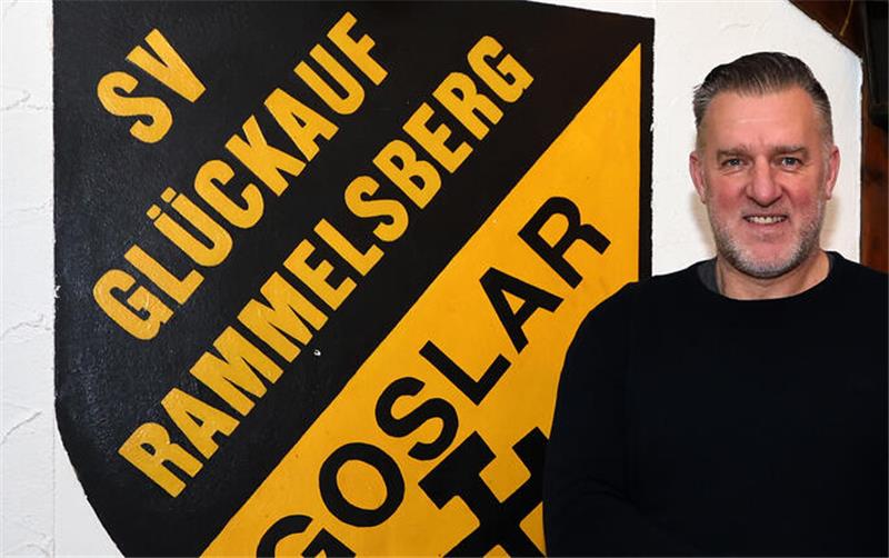 Ein Mann steht vor einer Wand mit einem gelb-schwarzen Wappenschild mit der Aufschrift 'SV Glückauf Rammelsberg Goslar