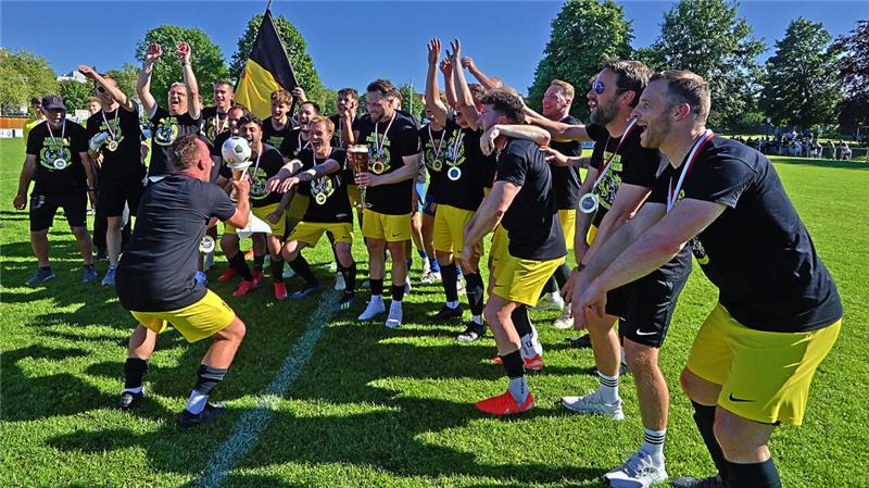 Fußballmannschaft in gelben Hosen und schwarzen Trikots feiert auf dem Spielfeld mit Pokal und Medaillen bei sonnigem Wetter