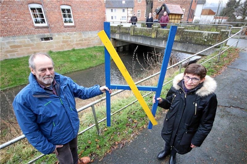 Joachim Kraume-Flügel und Roselyne Mijatovic halten an der Neilebrücke das mit gelben Balken durchgestrichene blaue H hoch, mit dem die Neuwallmodener „Hochwasserschutz jetzt“ fordern. Im Hintergrund weitere Mitglieder der Bürgerinitiative.  Foto: Gereke
