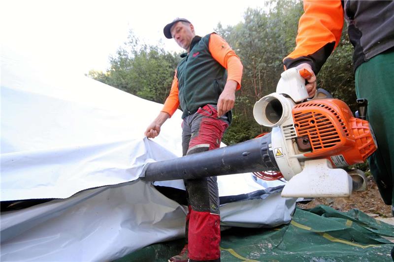 Jörg Müller (li.) hat ein Loch in das verschweißte Folienzelt rund um den Polter geschnitten. Mit einem Sauger ziehen nun die Forstmänner die Luft darunter heraus. Fotos: Gereke