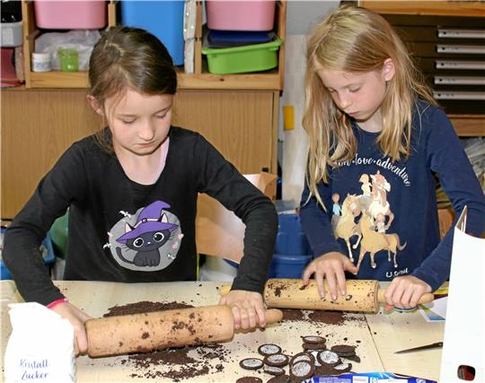 Johanna (links) und Ciara zerbröseln mithilfe eines Nudelholzes Oreo-Kekse für den Nachtisch. Summer und Anton (kleines Bild) bereiten den Kuchenteig vor und dürfen hinterher die Rührstäbe abschlecken. Foto: Knoke