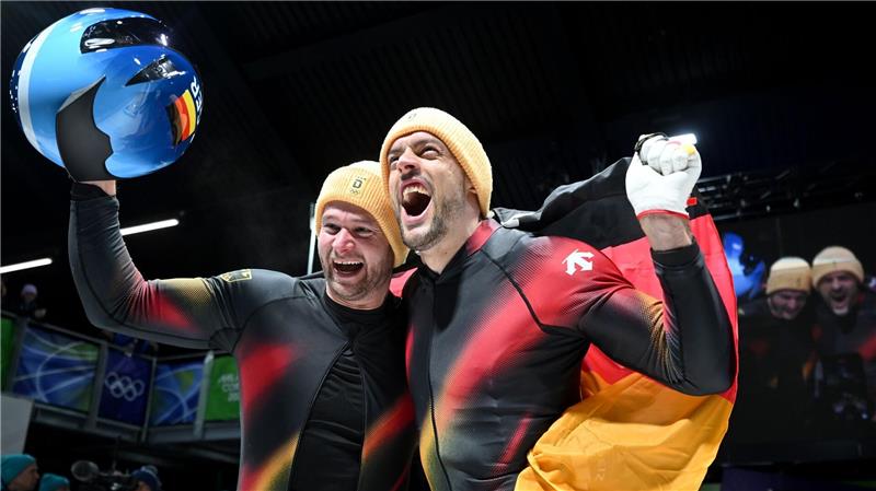 Johannes Lochner (Pilot, l) und Georg Fleischhauer bejubeln ihren ersten Platz im Zweierbob bei den Olympischen Winterspielen Mailand Cortina 2026.