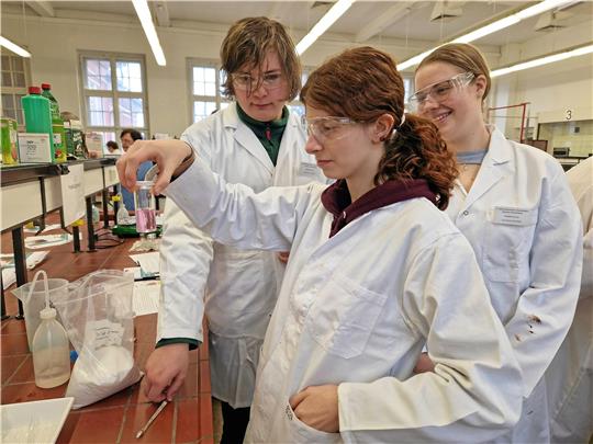 Jonas, Aurelia und Leonie (von links) experimentieren mit einer Wasser-Zucker-Lösung und Kaliumpermanganat. Foto: Knoke