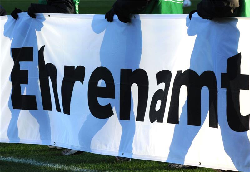 Jugendliche halten vor einem Fußball-Bundesligaspiel ein Banner mit der Aufschrift «Ehrenamt» in den Händen.