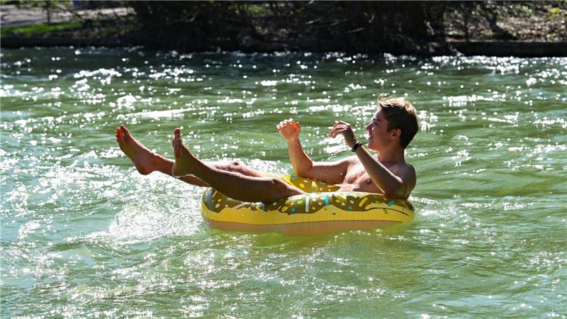 Julian treibt in einem aufblasbaren Donut im Eisbach im Englischen Garten in München. 