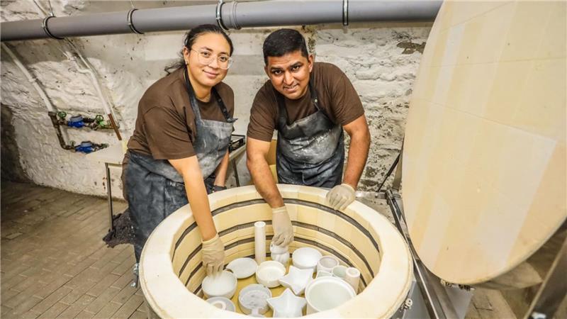 Julieth Andrea Bohorquez Ambrocio und Venkata Subramanian stehen an ihrem Brennofen, der mit Keramik gefüllt ist.