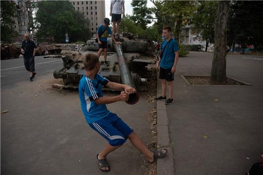Jungen spielen an einem zerstörten russischen Panzer, der auf einer Straße von Mykolajiw steht.