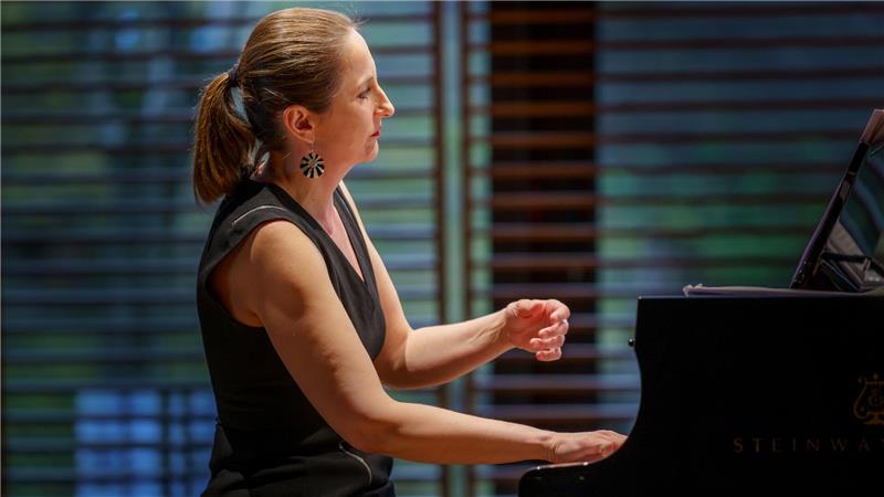 Frau mit Pferdeschwanz spielt Klavier in einem Raum mit Holzjalousien