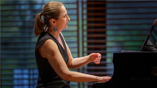 Frau mit Pferdeschwanz spielt Klavier in einem Raum mit Holzjalousien