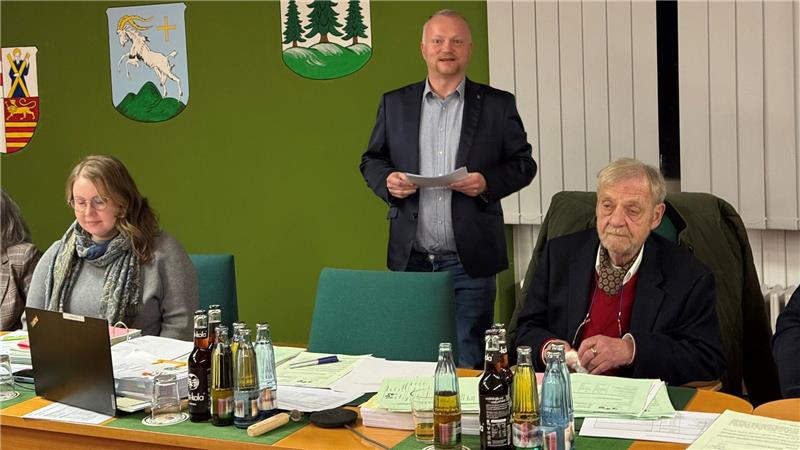 Das Foto zeigt einen stehenden Mann, der Notizen in der Hand hält und spricht.