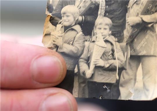 Kai Oppermann, in DDR-Kinderheimen groß geworden, zeigt ein Foto von seiner Einschulung. In der Bildmitte ist er in der vorderen Reihe mit Zuckertüte zu sehen. Links daneben steht sein Bruder Patrick.