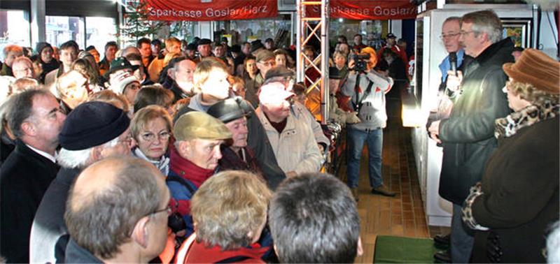 Hahnenklee rettet sich 2006 aus eigener Kraft und mit Goslarer Hilfe Menschenmenge in einem Innenraum, einige Personen hören einem Mann mit Mikrofon zu, der vor einem Banner mit der Aufschrift 'Sparkasse Goslar' spricht