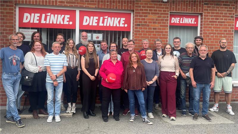 Gruppe von Menschen vor einem Backsteingebäude mit drei roten Schildern mit weißer Aufschrift 'DIE LINKE.'