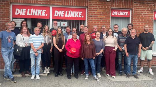 Gruppe von Menschen vor einem Backsteingebäude mit drei roten Schildern mit weißer Aufschrift 'DIE LINKE.'