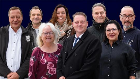 Acht Menschen, davon drei Frauen, stellen sich zum Gruppenbild auf und lächeln in die Kamera.