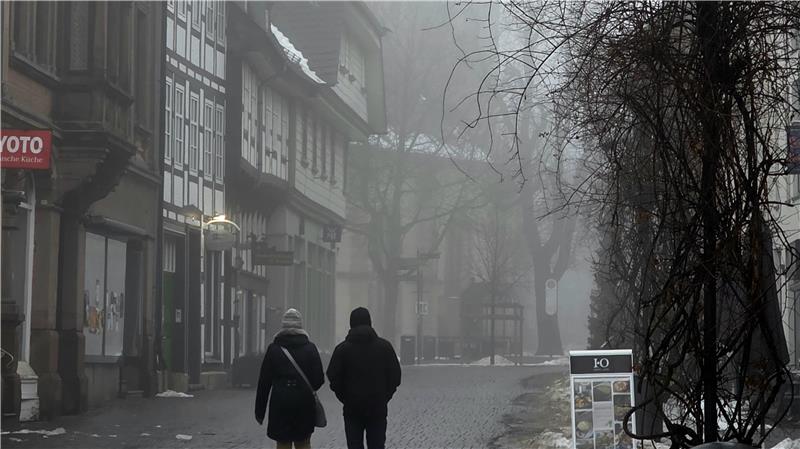 Zwei Personen gehen auf einer nebligen Kopfsteinpflasterstraße zwischen Fachwerkhäusern und kahlen Bäumen