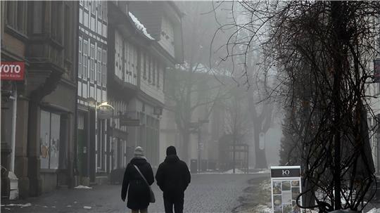 Zwei Personen gehen auf einer nebligen Kopfsteinpflasterstraße zwischen Fachwerkhäusern und kahlen Bäumen