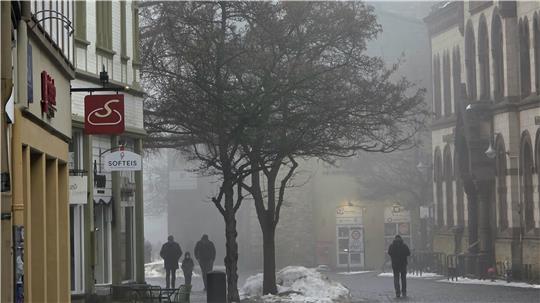 Zwei Personen gehen auf einer nebligen Kopfsteinpflasterstraße zwischen Fachwerkhäusern und kahlen Bäumen