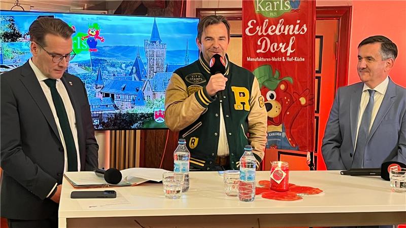 30-Millionen-Projekt: Karls Erlebnisdorf eröffnet 2028 in Wernigerode Ein Mann steht an einem Tisch und spricht in ein Mikrofon, zwei weitere Männer hören ihm zu.