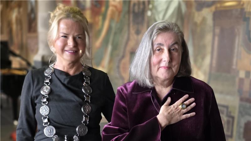 Das Foto zeigt die Kaiserringträgerin Katharina Fritsch auf der rechten Seite mit Oberbürgermeisterin Urte Schwerdtner auf der linken Seite. Katharina Fritsch präsentiert den Kaiserring an ihrer rechten Hand.