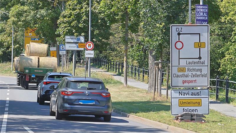 Straße mit mehreren Fahrzeugen, darunter ein Traktor mit Heuballen, und einem großen Verkehrsschild mit Umleitungsinformationen für Lautenthal und Clausthal-Zellerfeld