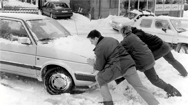 Drei Menschen schieben ein Auto aus dem Schnee heraus.
