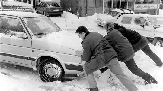 Drei Menschen schieben ein Auto aus dem Schnee heraus.