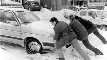 Drei Menschen schieben ein Auto aus dem Schnee heraus.