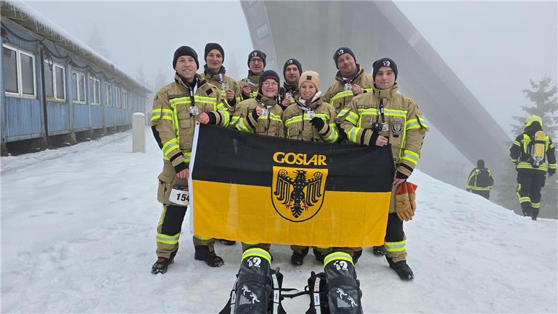 Mehrere Feuerwehrleute posieren für ein Foto und halten eine Flagge mit dem Goslarer Stadtzeichen in der Hand. 