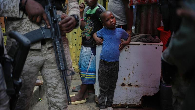 Kind neben bewaffnetem Polizisten in Unterkunft für Vertriebene in Port-au-Prince
