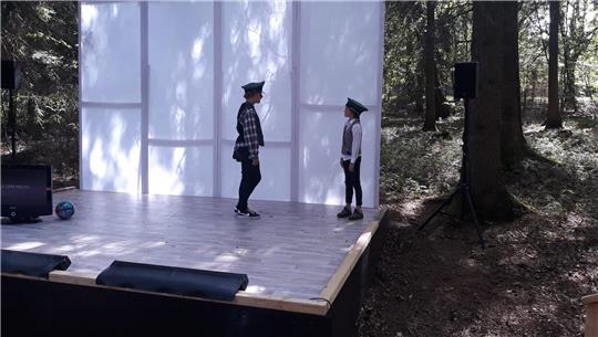 Das Foto zeigt zwei Kinder auf einer Bühne mitten im Wald.