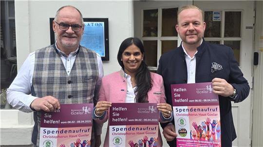 Drei Personen stehen vor einem Gebäude und halten jeweils ein Plakat mit der Aufschrift 'Spendenaufruf' und bunten Händen darauf.